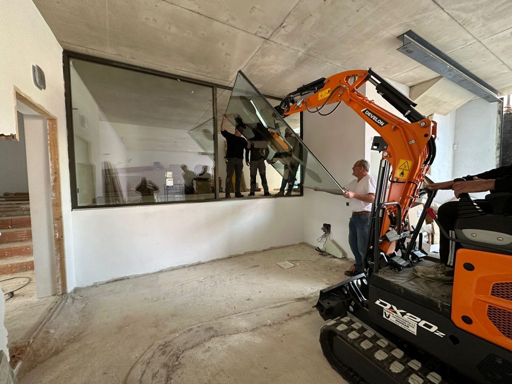 Develon Mini-Excavator Used To Install Panes of Glass In Home